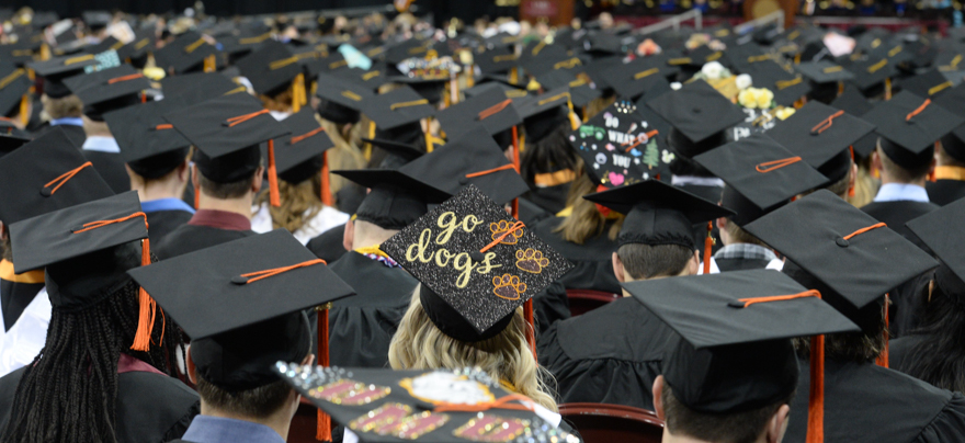 Students face the front of the auditorium with their graduation caps and gowns on.