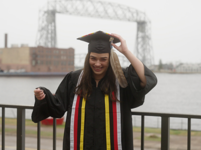 Student in cap and gown in front of the Aerial Lift Bridge